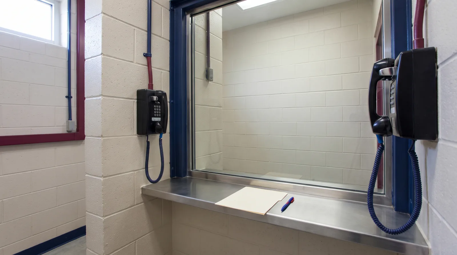 Secure correctional facility visiting booth with a glass partition, wall phones and a document on the counter